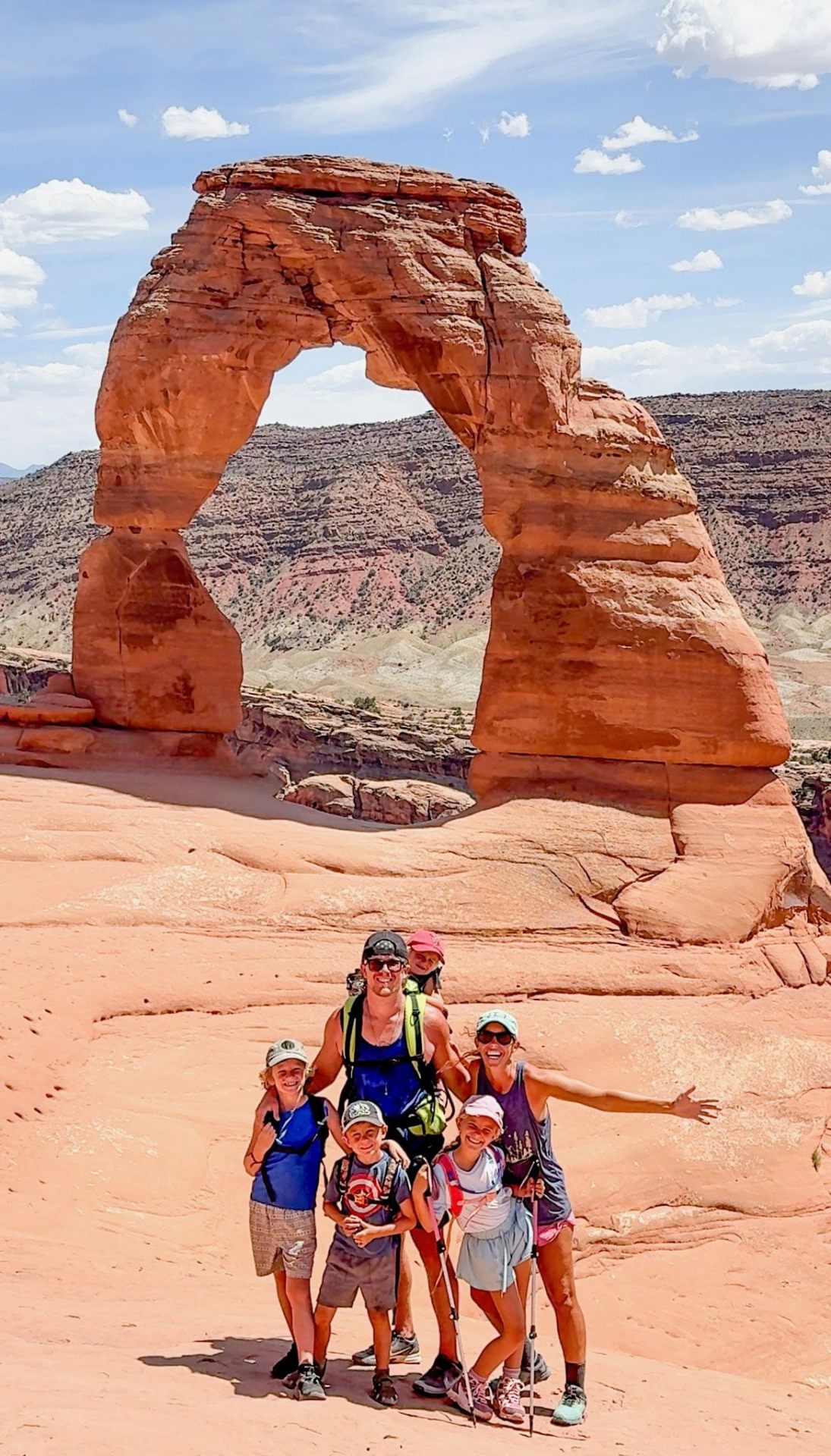 A family standing together beneath Delicate Arch at dusk